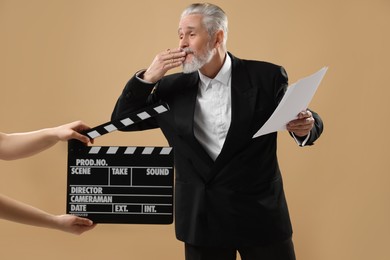 Photo of Senior actor performing role while second assistant camera holding clapperboard on beige background. Film industry