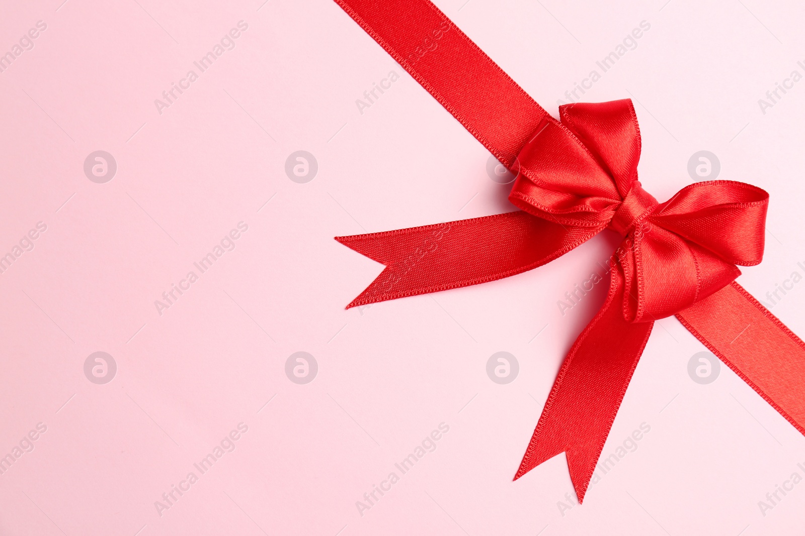 Photo of Red ribbon with bow on color background, top view