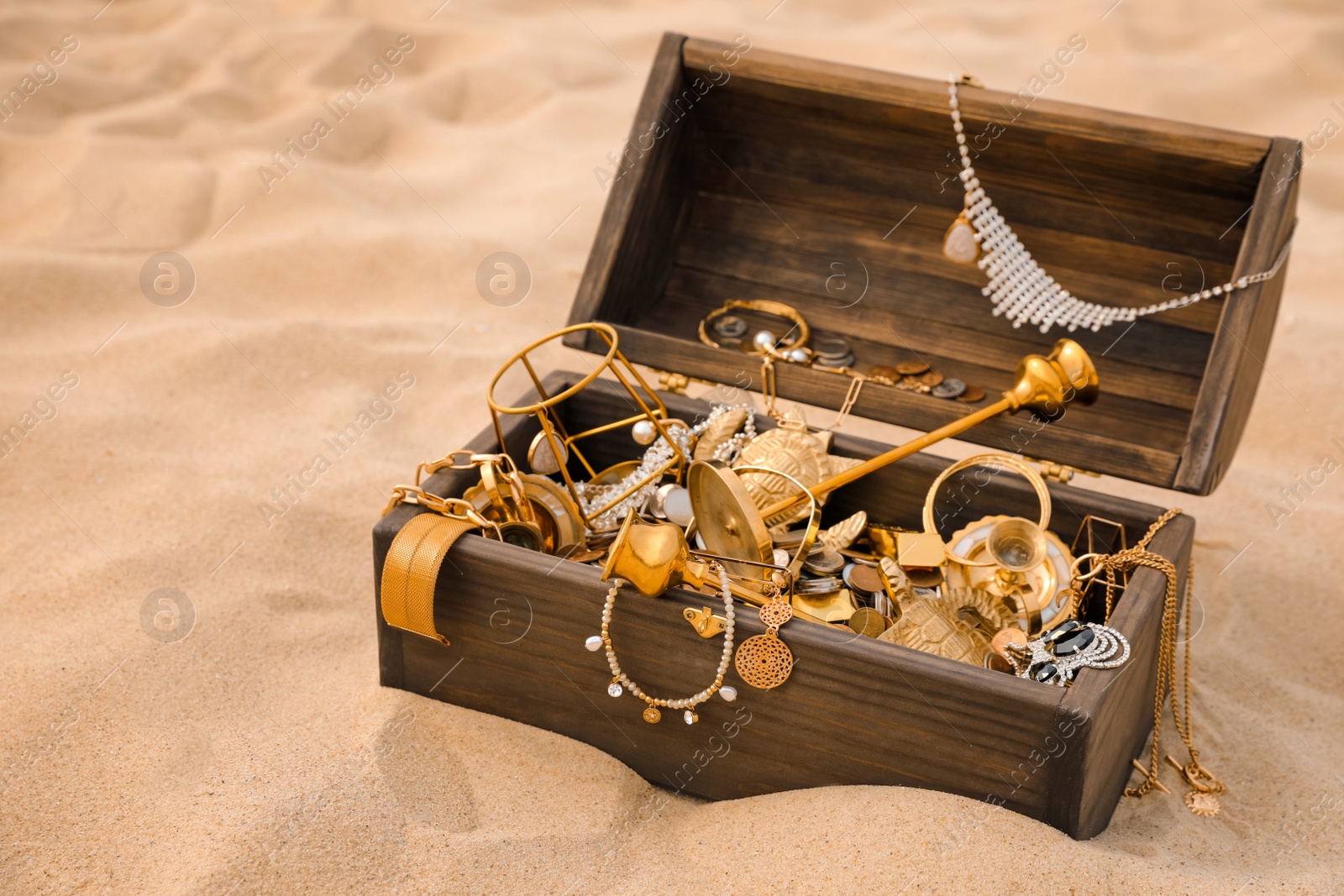 Photo of Open wooden chest with treasures on sand