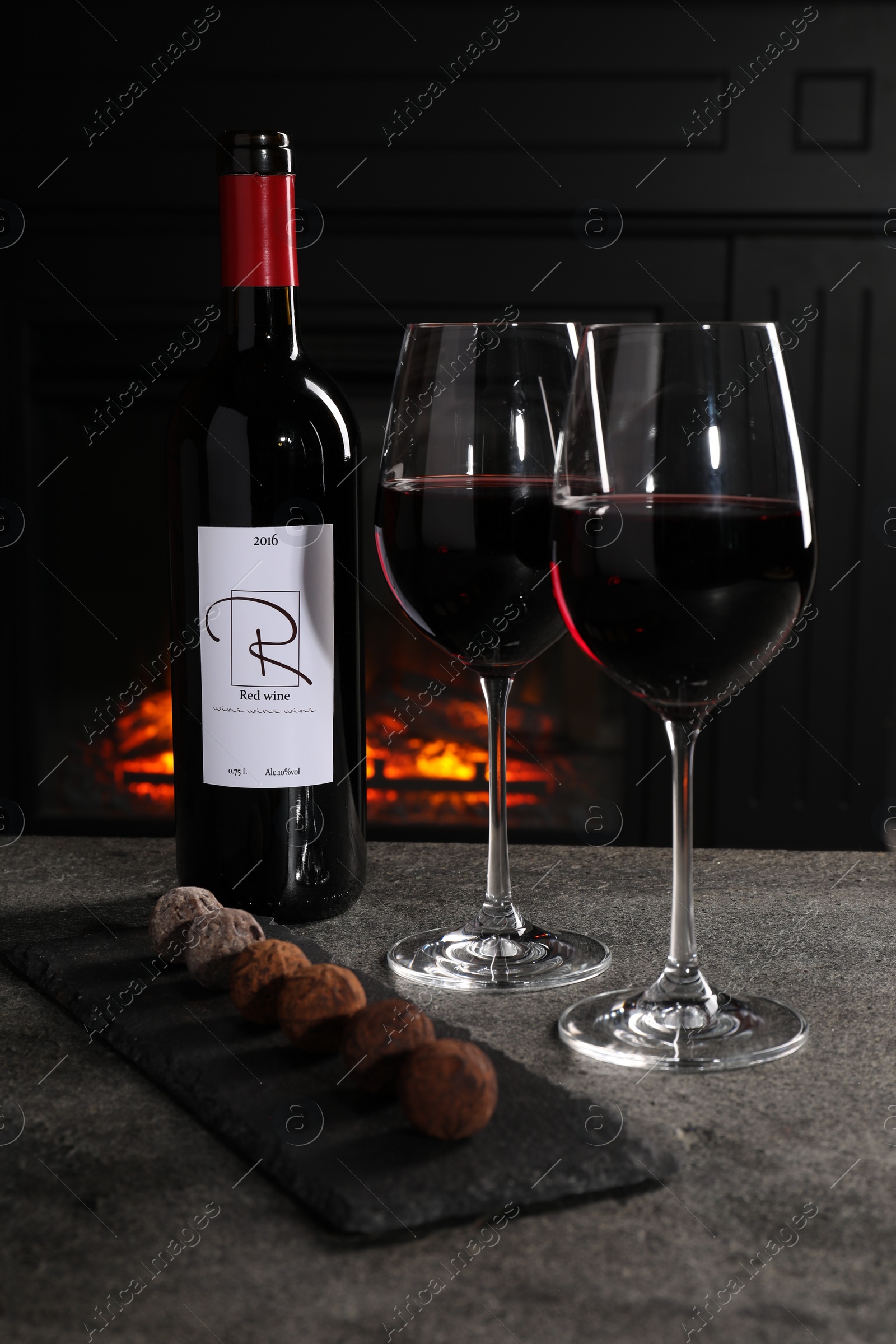 Photo of Red wine and chocolate truffles on gray table against fireplace