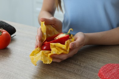 Photo of Woman packing half of bell pepper into beeswax food wrap at wooden table indoors, closeup