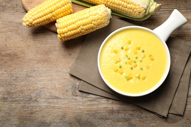 Photo of Delicious creamy corn soup and cobs on wooden table, flat lay. Space for text
