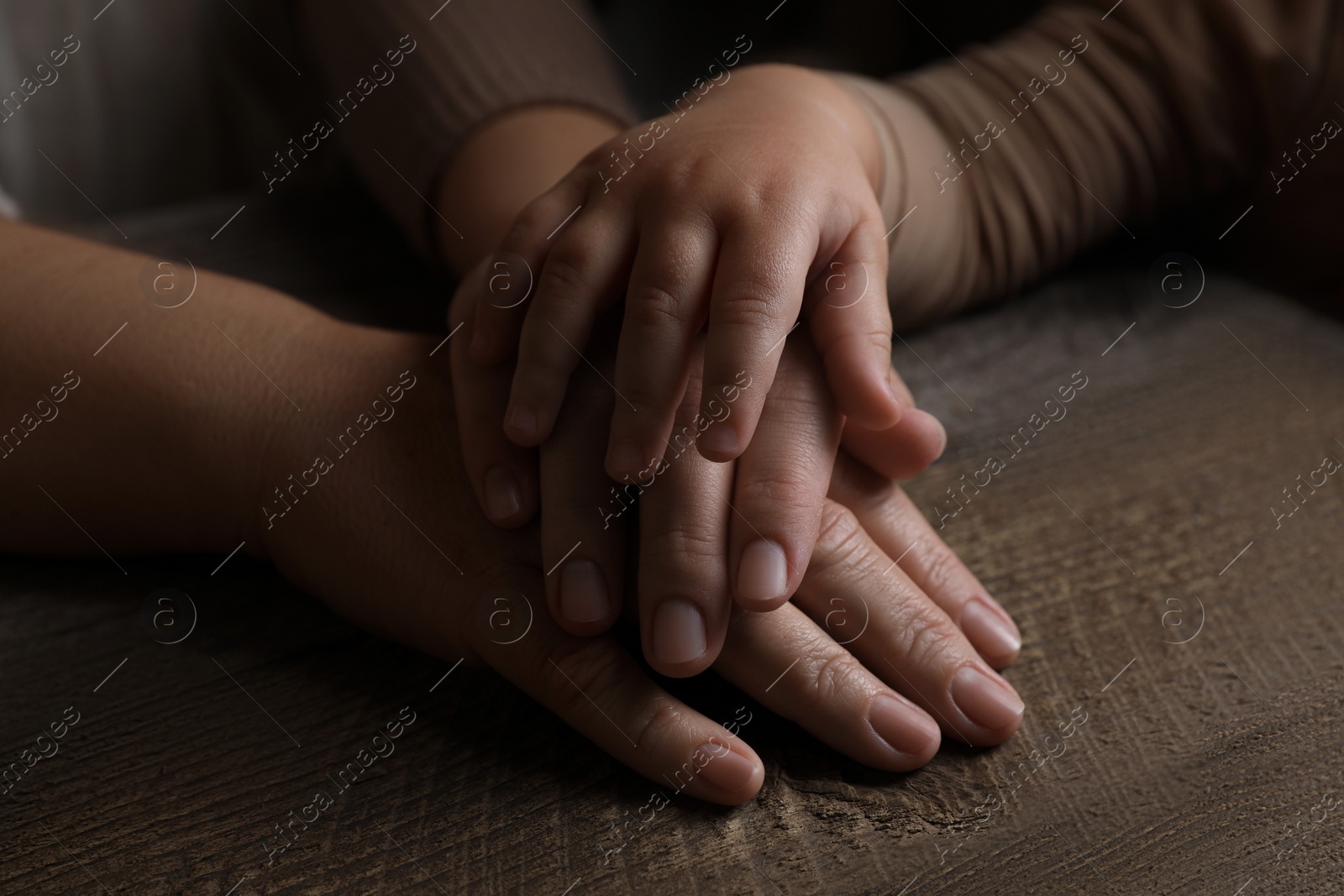 Photo of Family holding hands together at wooden table, closeup