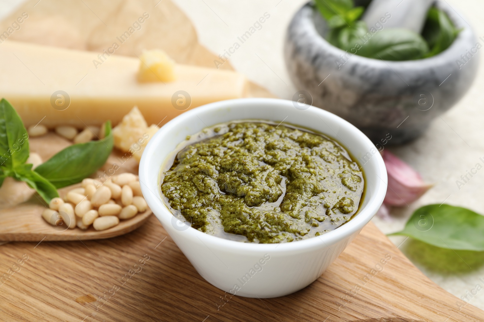 Photo of Tasty pesto sauce in bowl, basil, pine nuts and cheese on table, closeup