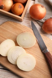 Photo of Whole and sliced onions on white wooden table, flat lay