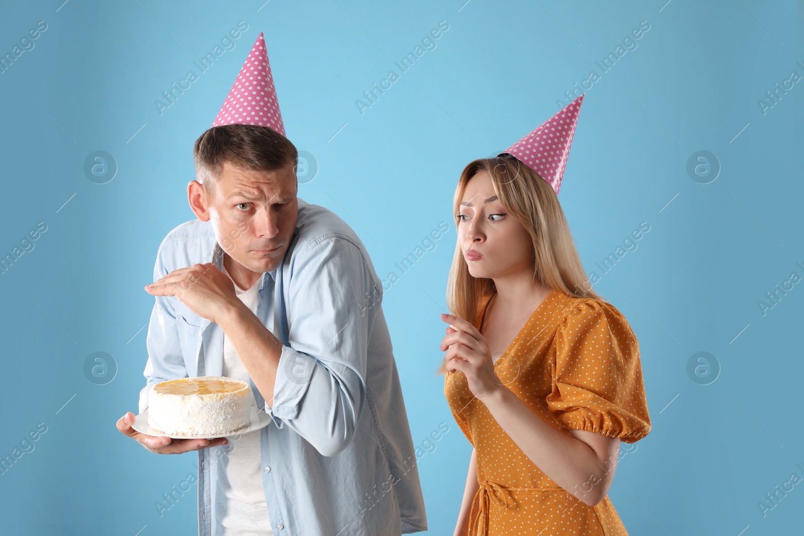 Photo of Greedy man hiding birthday cake from woman on turquoise background