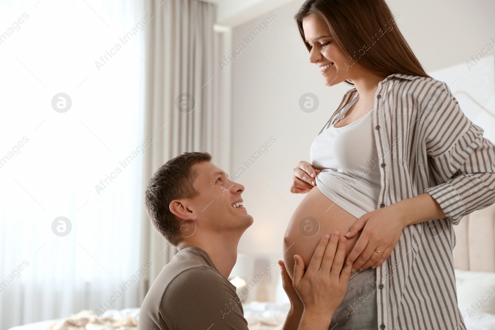 Photo of Young pregnant woman with her husband in bedroom