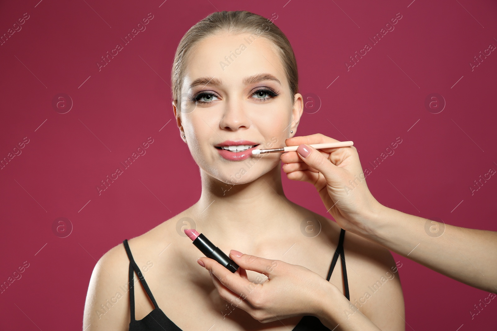 Photo of Artist applying makeup onto woman's face on pink background