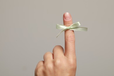 Woman showing index finger with tied bow as reminder on grey background, closeup