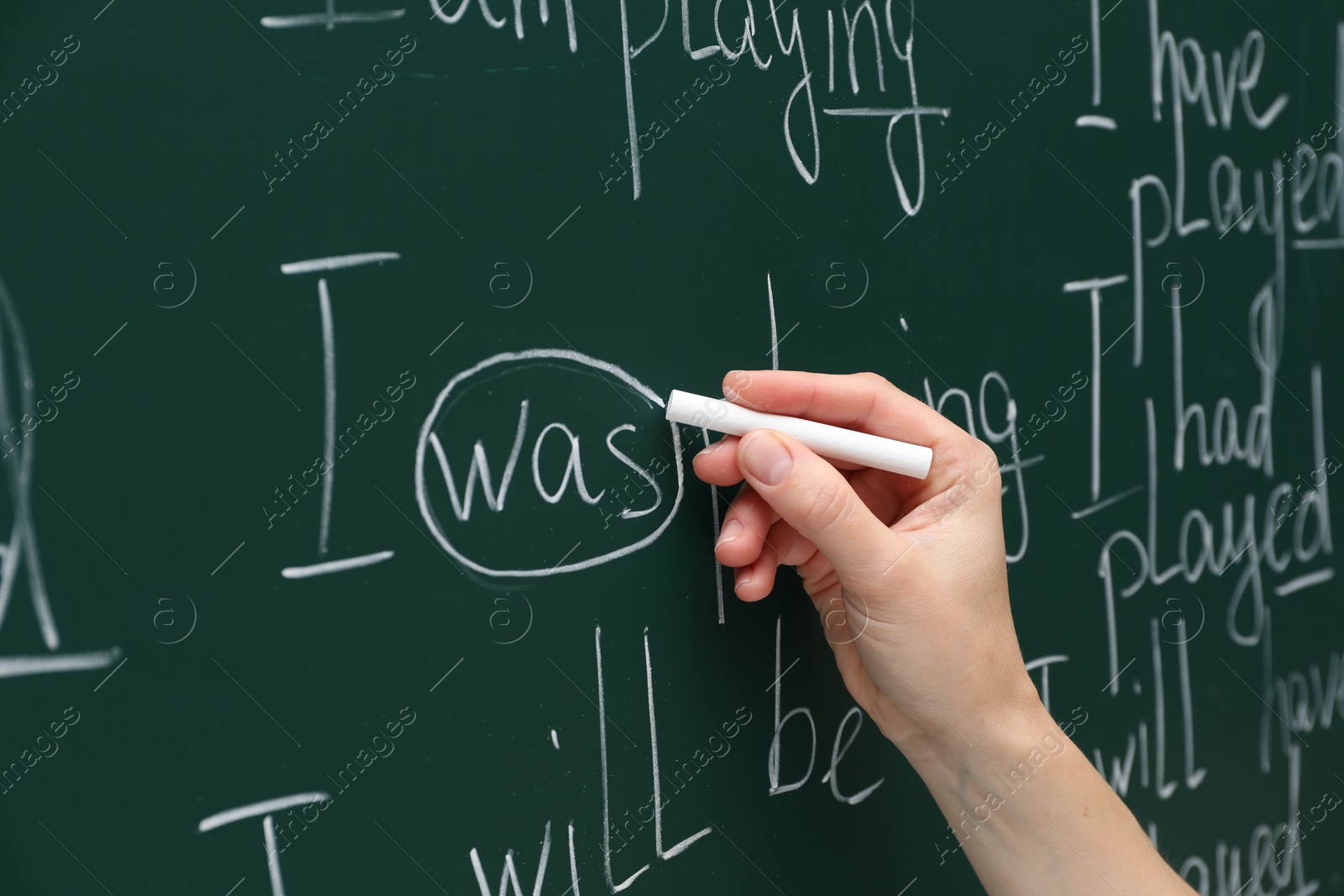 Photo of English teacher writing with chalk on green chalkboard, closeup