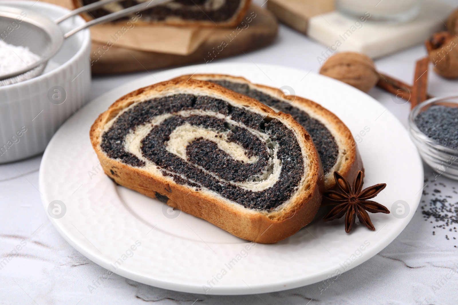 Photo of Slices of poppy seed roll and anise star on white textured table, closeup. Tasty cake