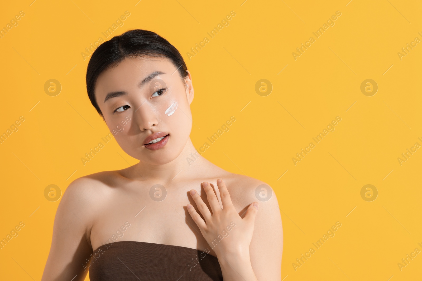 Photo of Beautiful young woman with sun protection cream on her face against orange background, space for text