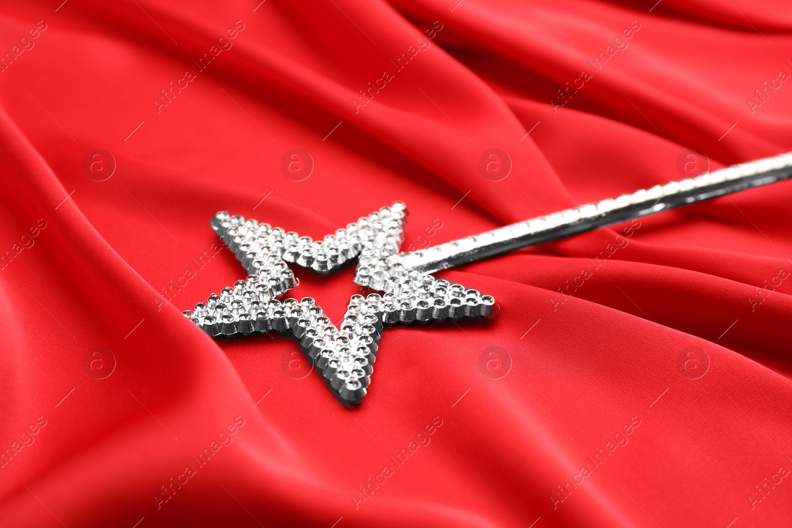 Photo of Beautiful silver magic wand on red fabric, closeup
