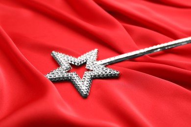 Photo of Beautiful silver magic wand on red fabric, closeup