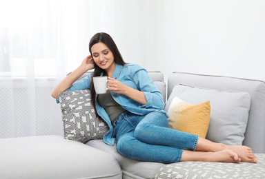 Young woman with cup of drink relaxing on couch at home