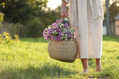 Photo of Woman holding wicker basket with beautiful wild flowers outdoors, closeup