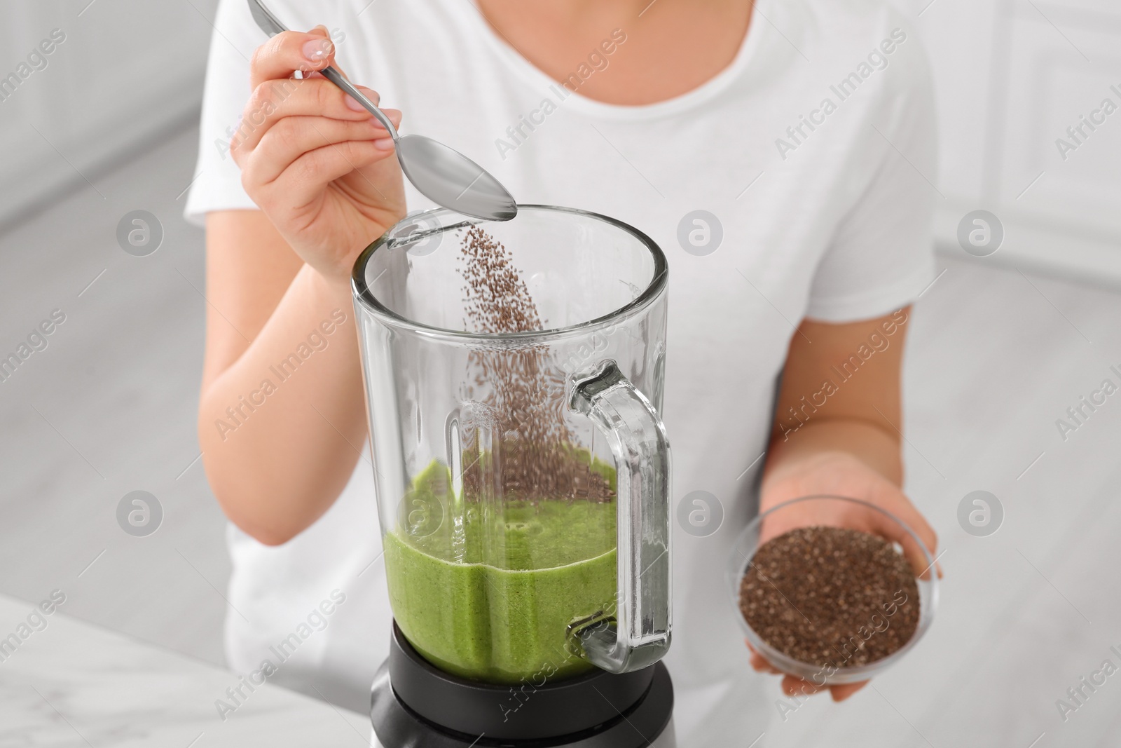 Photo of Woman adding chia seeds into blender with delicious smoothie in kitchen, closeup