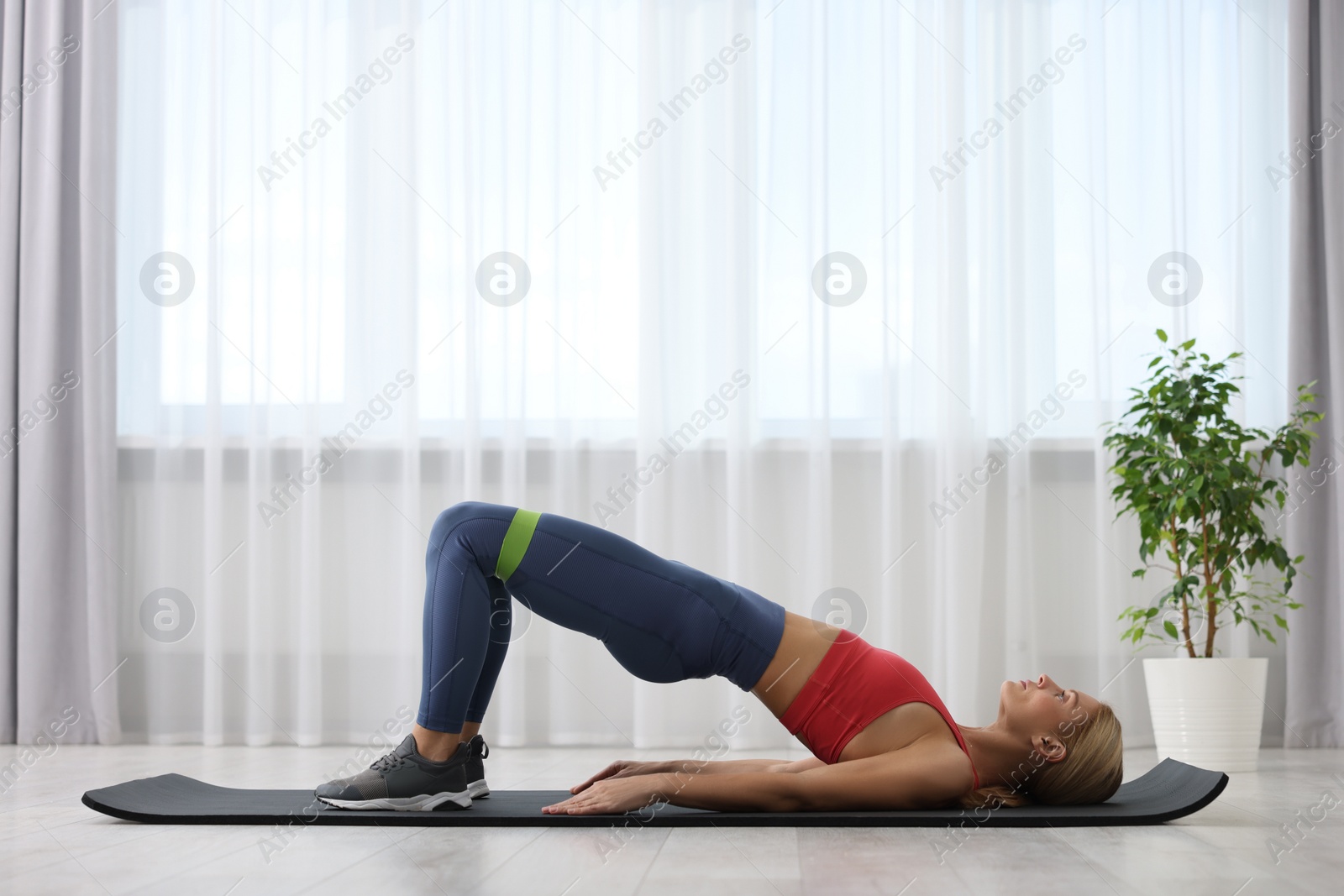 Photo of Athletic woman doing exercise with fitness elastic band on mat at home