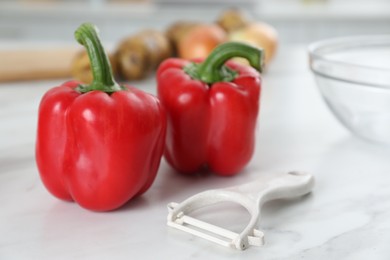 Photo of Red bell peppers and peeler on white marble table, closeup