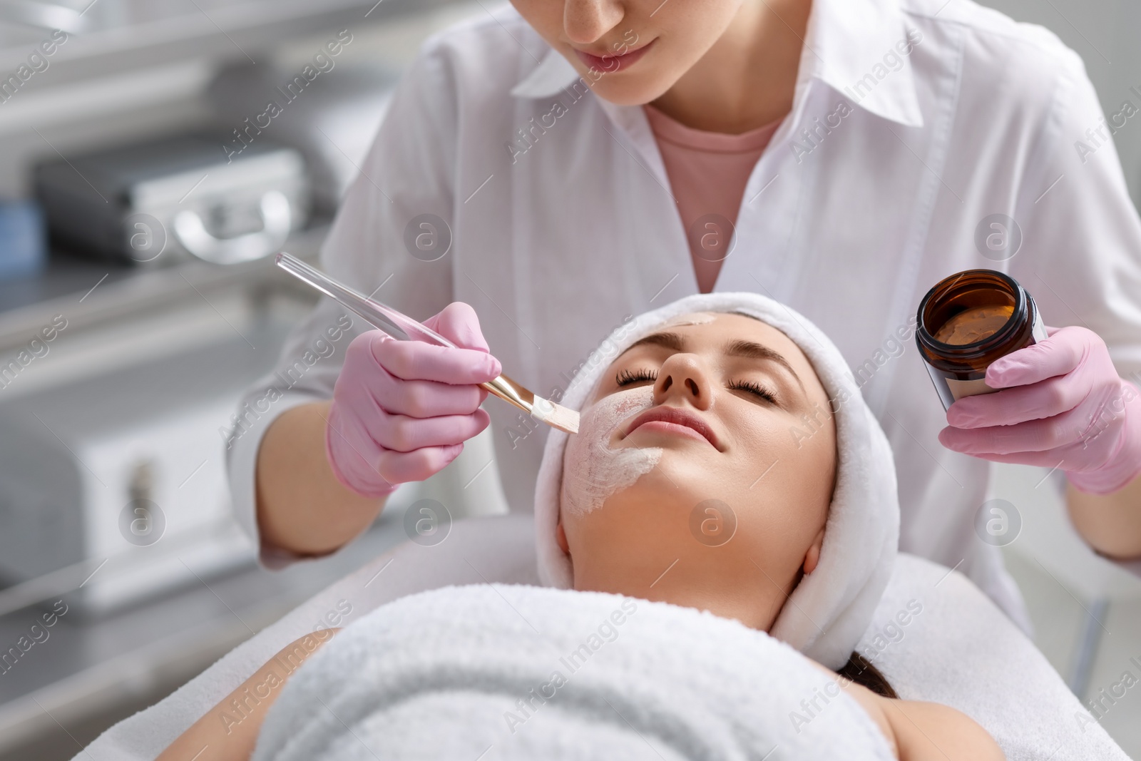 Photo of Cosmetologist applying mask on woman's face in clinic, closeup