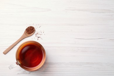 Photo of Freshly brewed rooibos tea, dry leaves and spoon on white wooden table, flat lay. Space for text