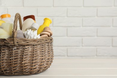 Photo of Wicker basket full of different baby cosmetic products, accessories and toy on white wooden table. Space for text