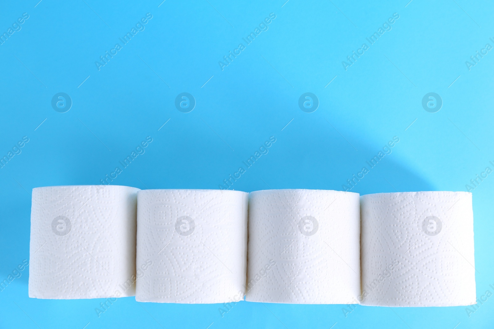 Photo of Soft toilet paper rolls on light blue background, flat lay. Space for text