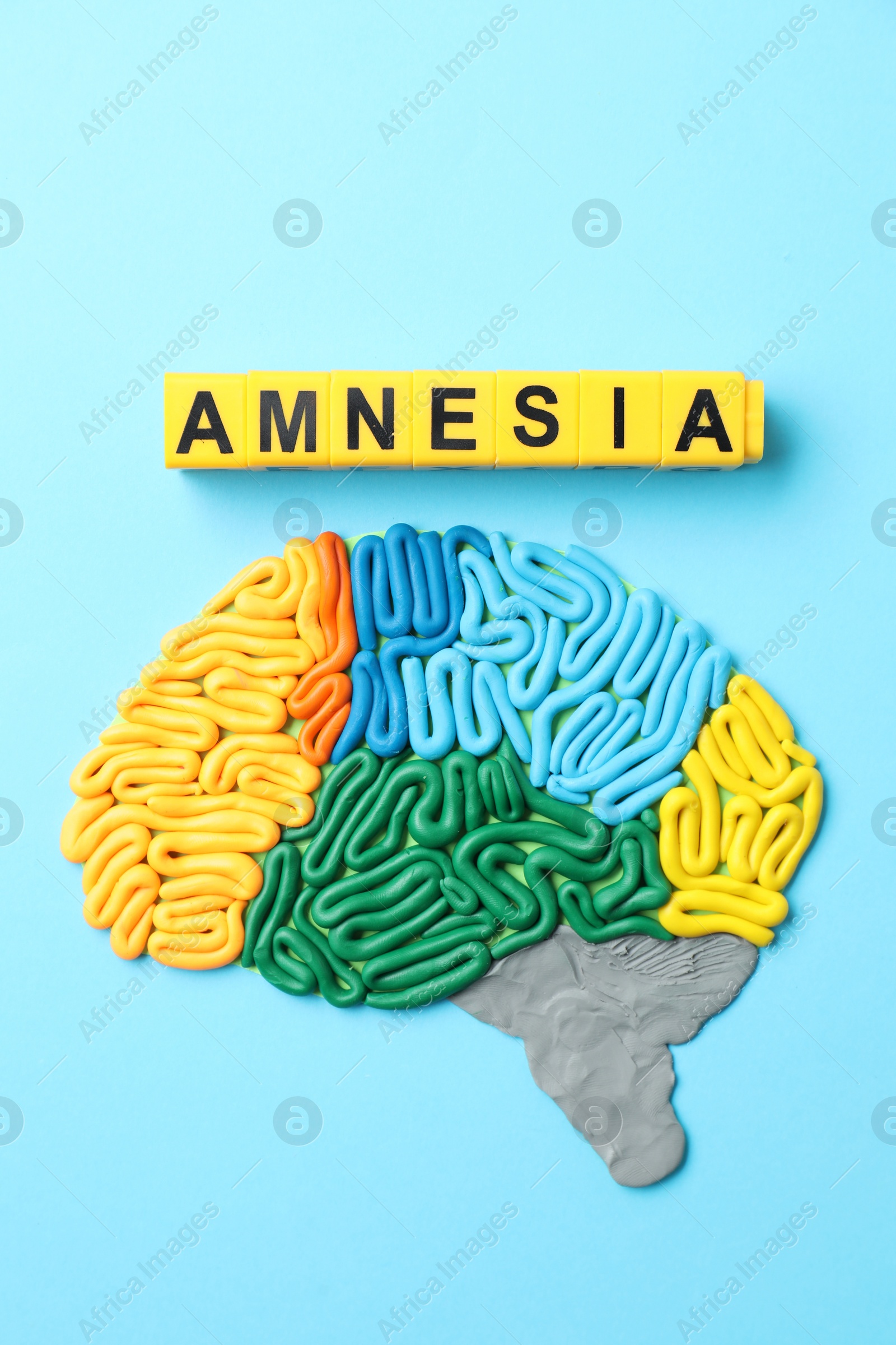 Photo of Word Amnesia and brain with sections made of plasticine on light blue background, flat lay