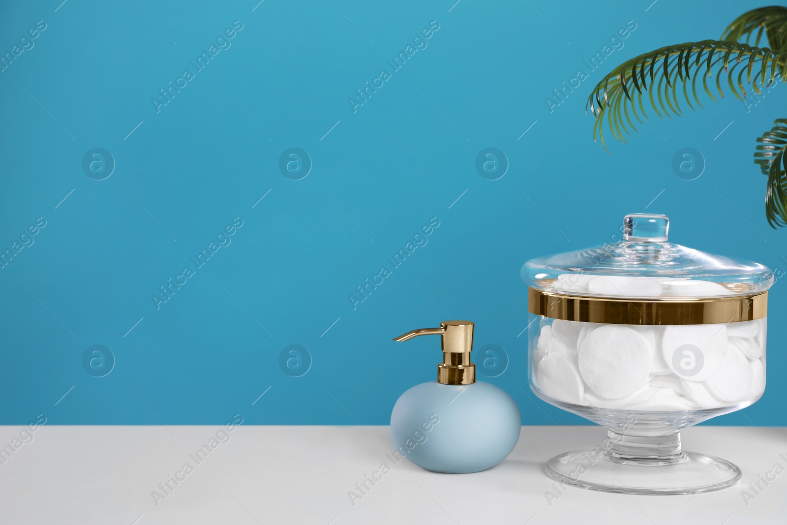 Photo of Jar with cotton pads on white table against blue background. Space for text