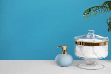 Jar with cotton pads on white table against blue background. Space for text