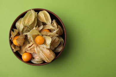 Ripe physalis fruits with calyxes in bowl on green background, top view. Space for text