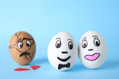 Photo of Eggs with drawn faces on light blue background. Concept of jealousy