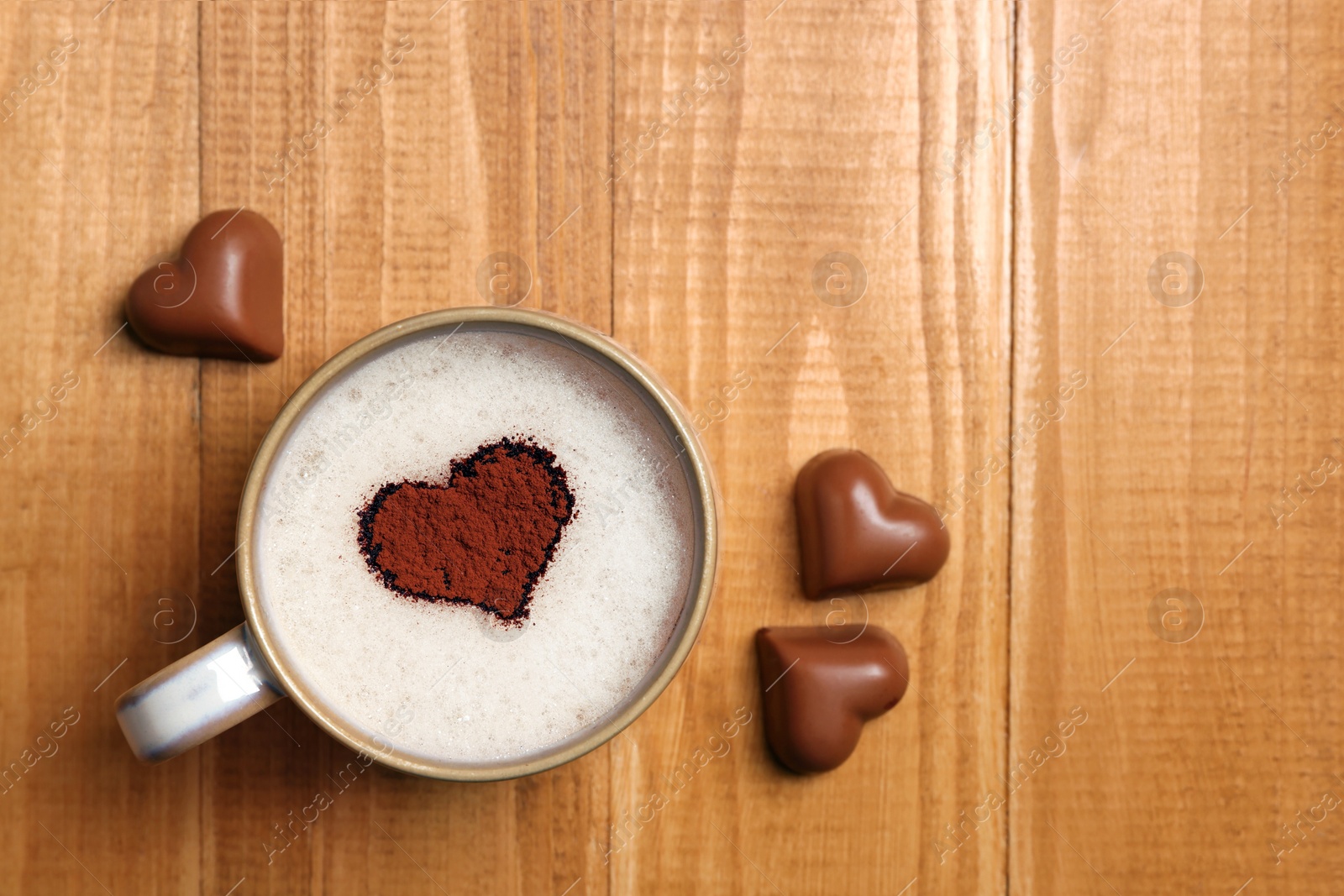 Photo of Cup of aromatic coffee with heart shaped decoration and chocolate candies on wooden table, flat lay. Space for text