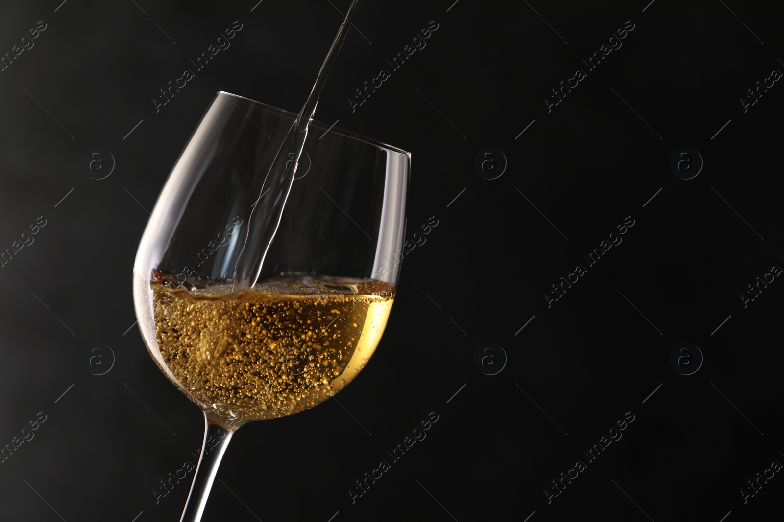 Photo of Pouring white wine into glass on dark background. Space for text