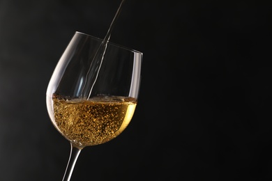 Photo of Pouring white wine into glass on dark background. Space for text