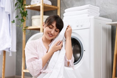 Photo of Young housewife with laundry near washing machine at home
