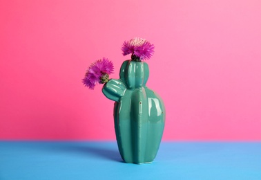 Photo of Trendy cactus shaped ceramic vase with flowers on table against color background