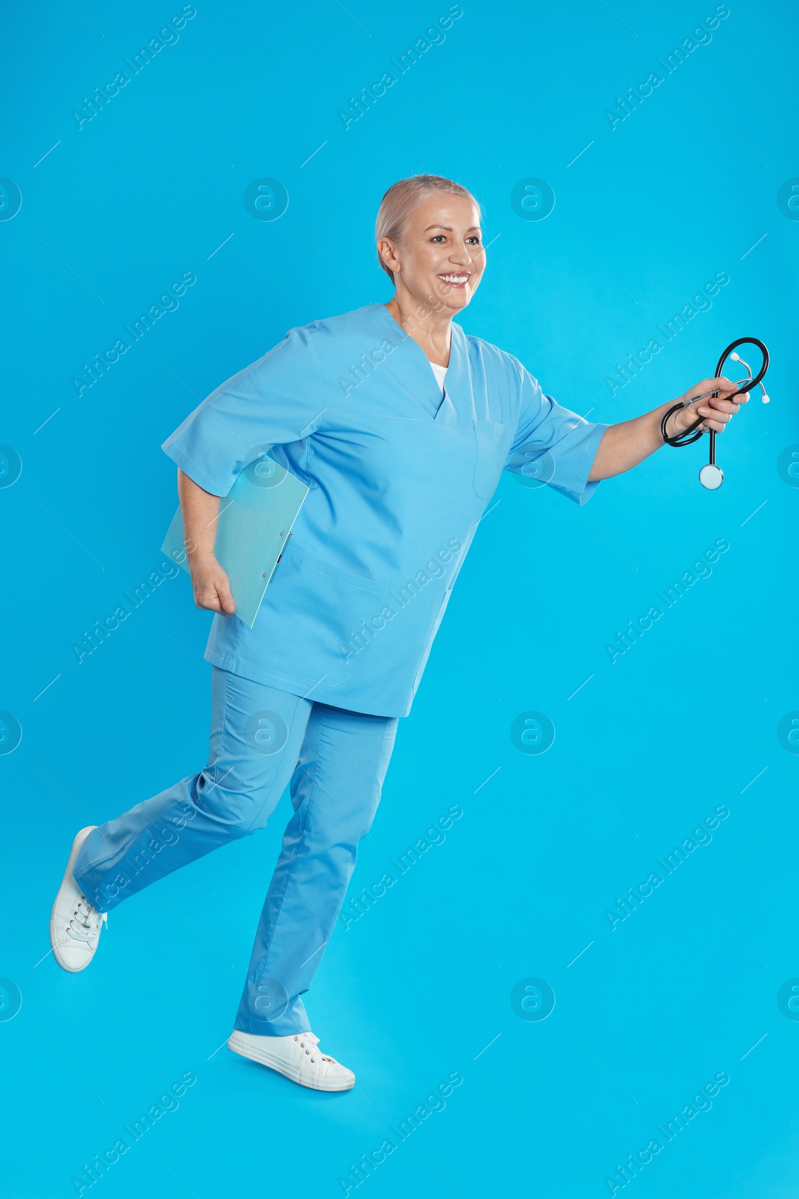 Photo of Mature doctor in uniform running on blue background