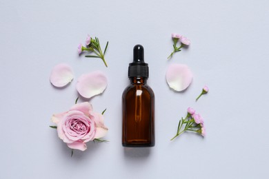 Bottle of cosmetic serum and beautiful flowers on light grey background, flat lay