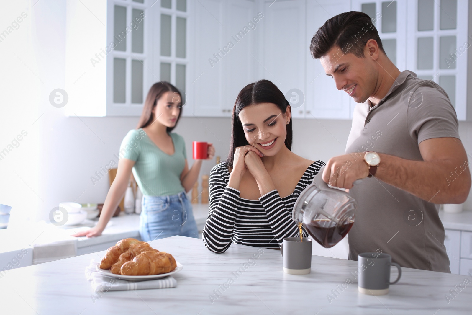 Photo of Unhappy woman feeling jealous, focus on couple spending time together in kitchen