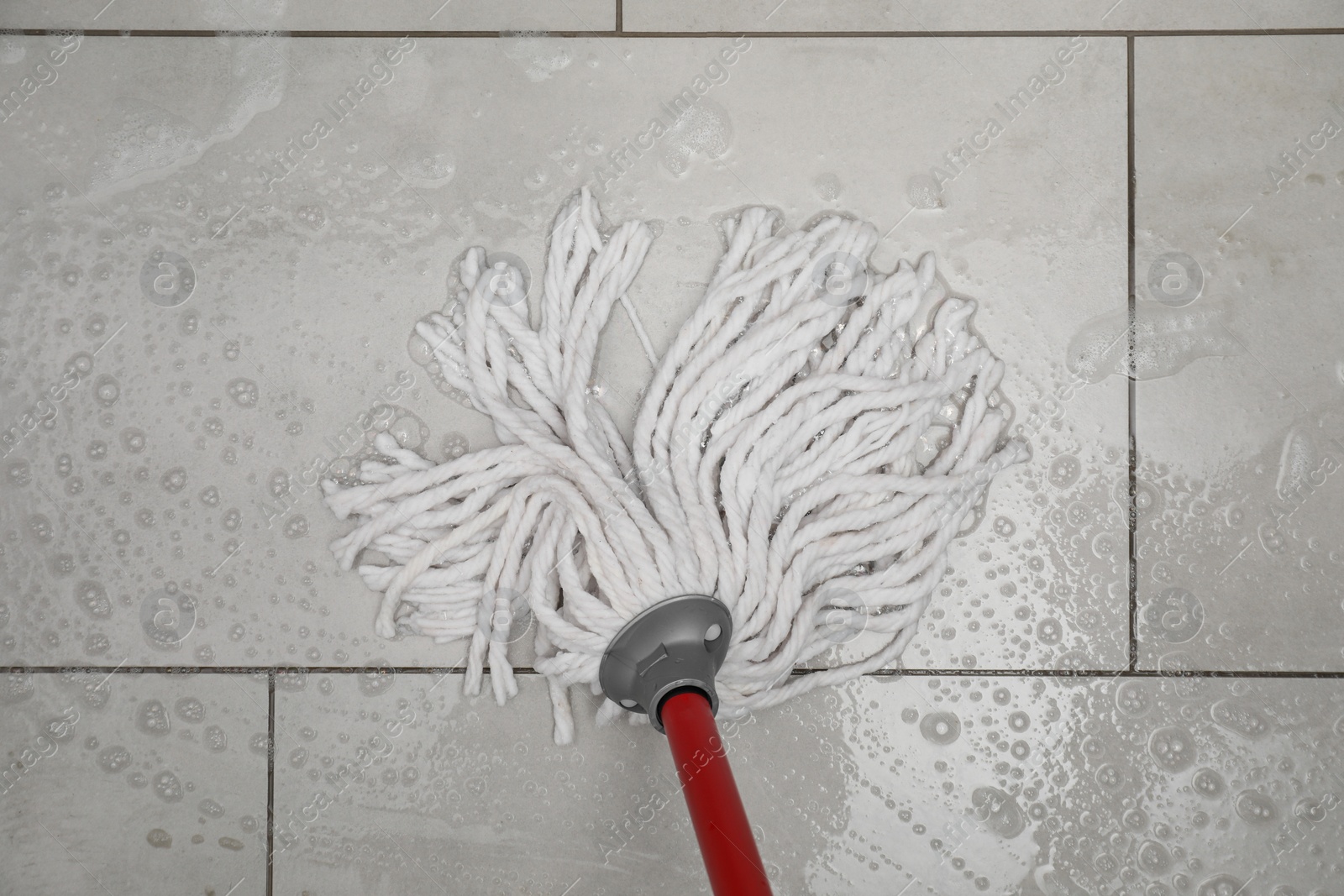 Photo of Cleaning grey tiled floor with string mop, top view