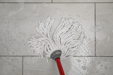 Photo of Cleaning grey tiled floor with string mop, top view