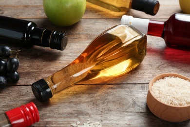 Bottles with different kinds of vinegar and ingredients on wooden table