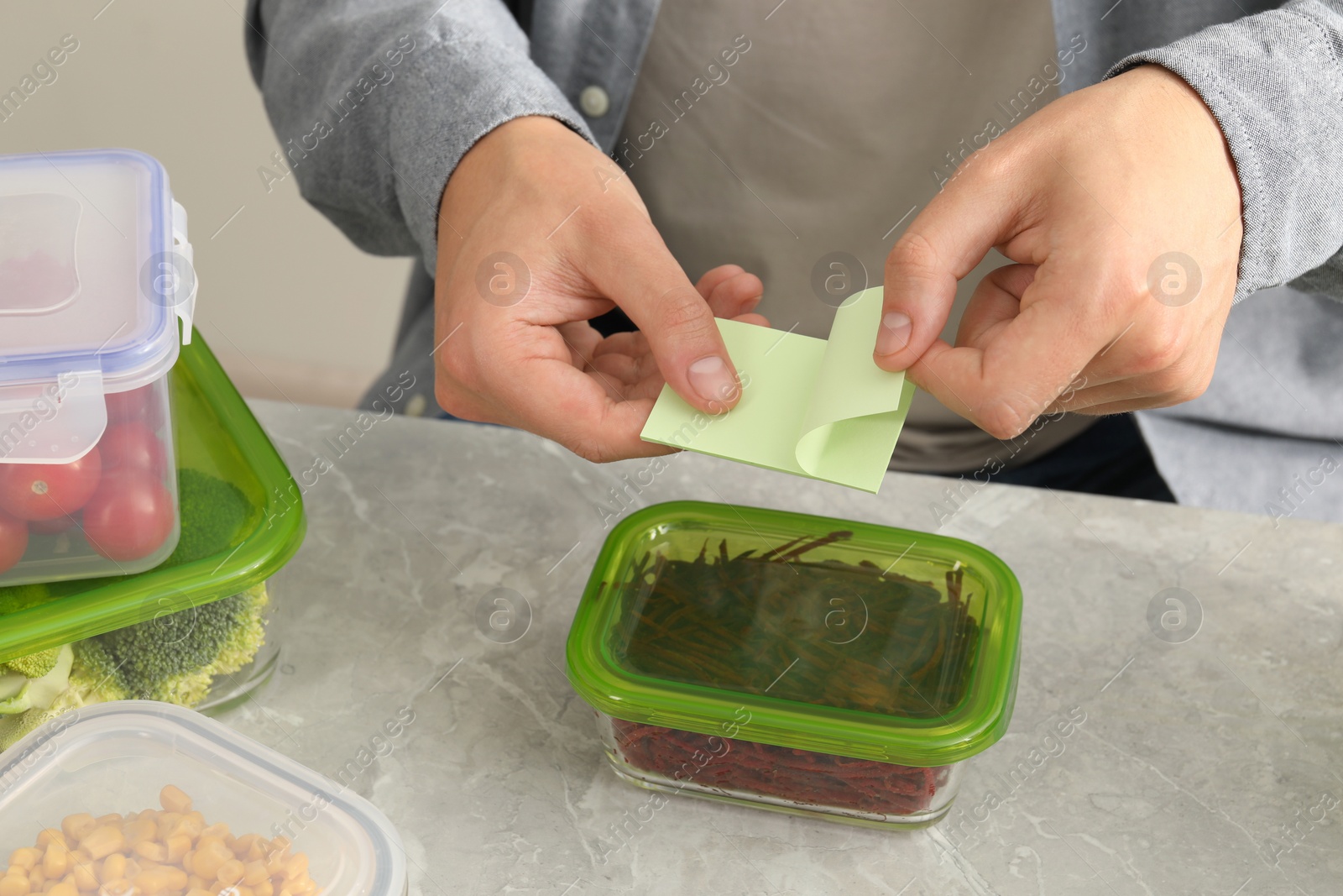 Photo of Man sticking paper note onto container with cut beets at light grey table, closeup. Food storage