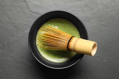 Photo of Cup of fresh green matcha tea with bamboo whisk on black table, top view