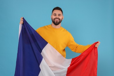 Photo of Young man holding flag of France on light blue background