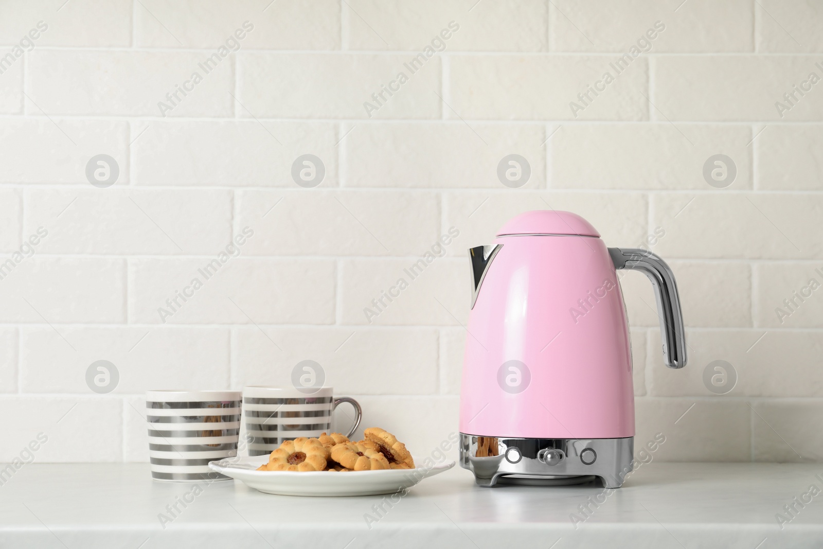 Photo of Modern electric kettle, cups and cookies on counter in kitchen