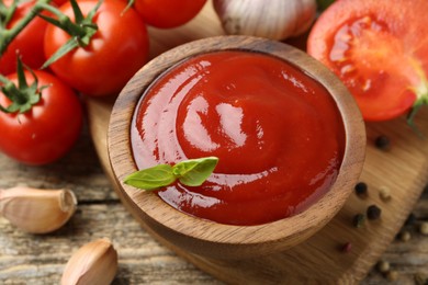 Tasty ketchup, fresh tomatoes, basil and spices on wooden table, closeup