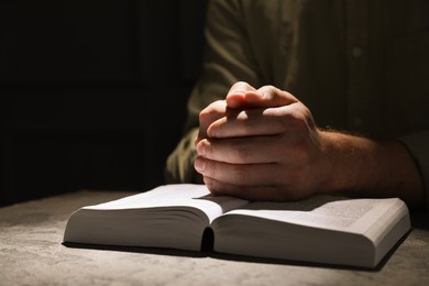 Photo of Religion. Christian man praying over Bible at table, closeup. Space for text