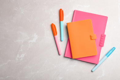 Image of Stylish pink and orange notebooks, pens on marble table, flat lay. Space for text